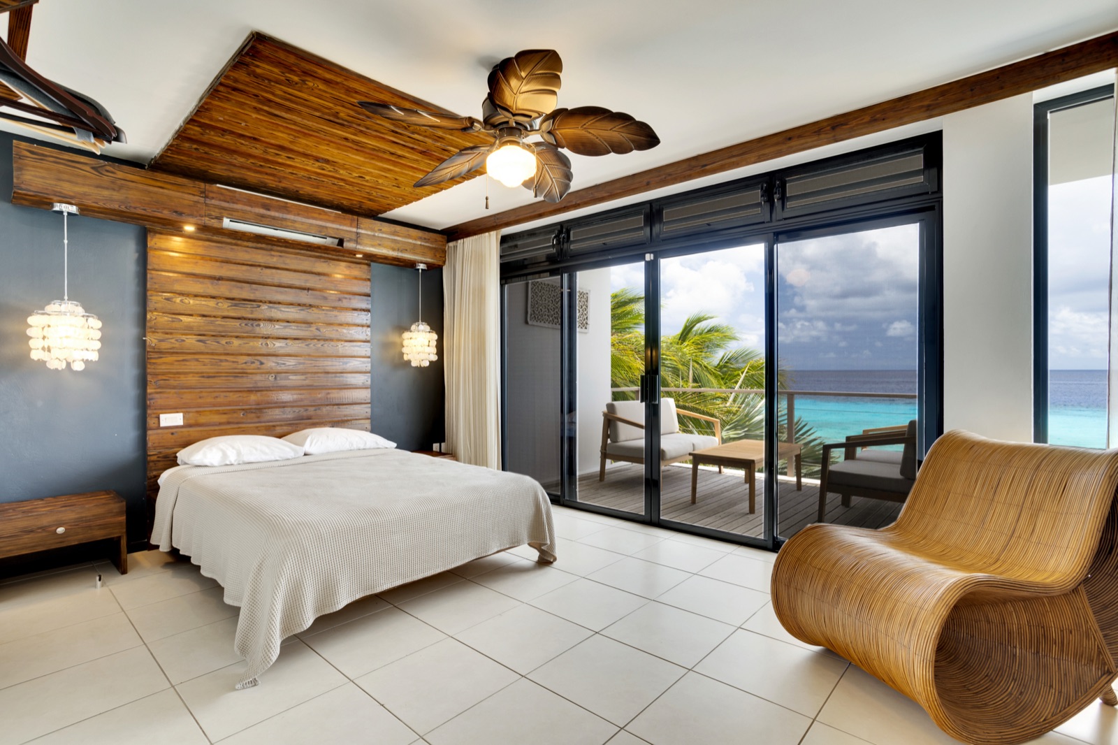 Luxury Bonaire villa master bedroom with a large natural wood headboard, private oceanfront balcony, and panoramic views of the turquoise Caribbean Sea.